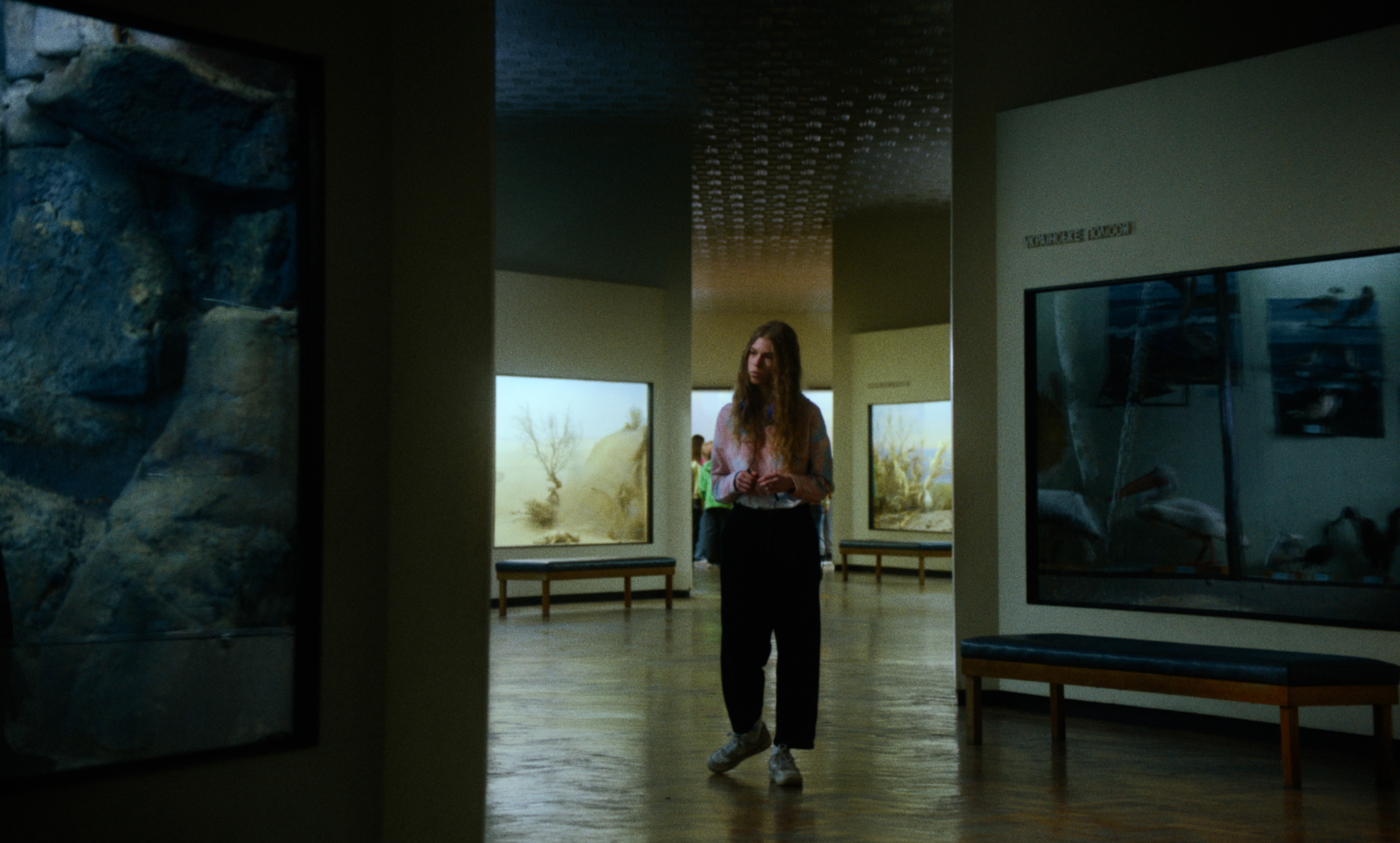 A young woman walks alone through a museum gallery with large exhibits — a still from Kira’s Dream.