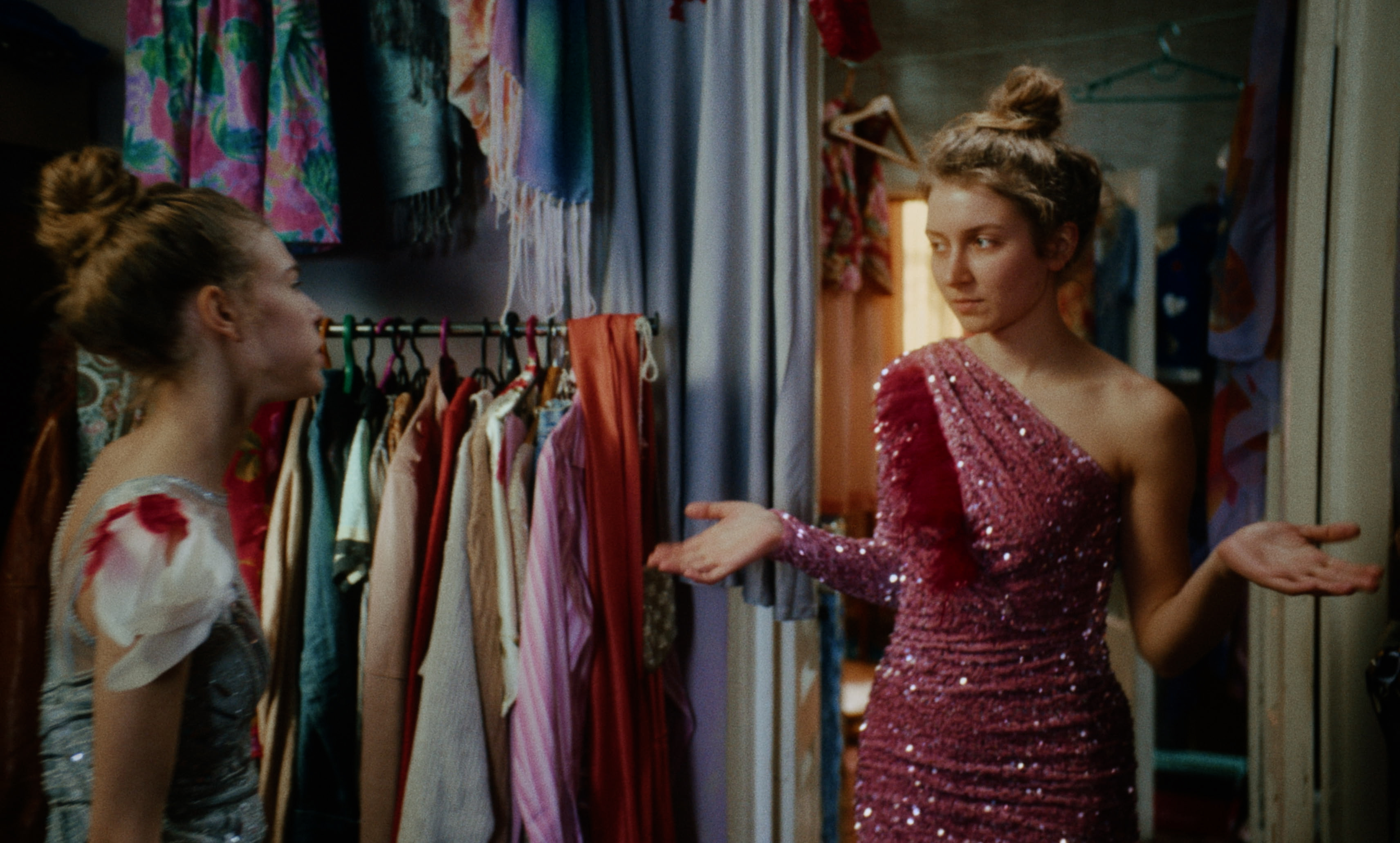 Two young women talk in a costume room; one wears a pink sequined dress — a still from Kira’s Dream.