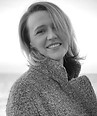 Black and white portrait of a smiling woman in a textured coat.