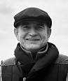 Smiling man in a flat cap and jacket, black and white photo.