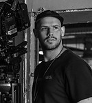 Cinematographer standing beside large camera rig on a film set backdrop.