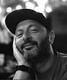 Bearded man in cap smiling, resting head, black and white photo.